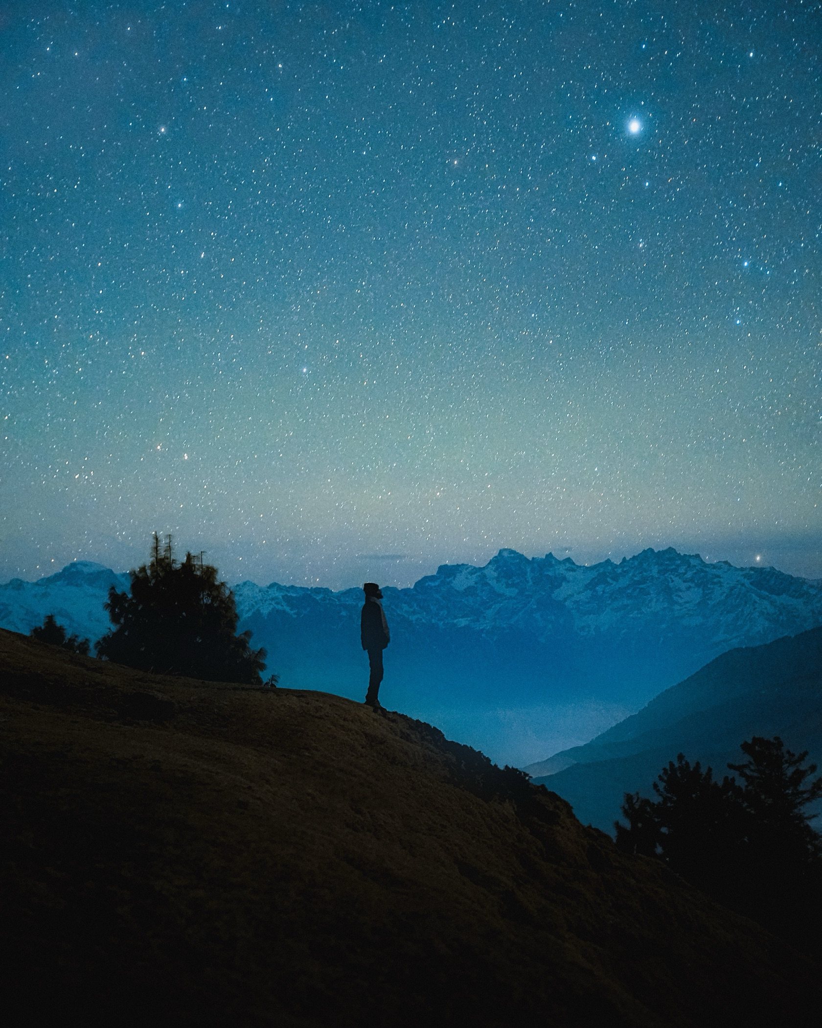 A person looking up at stars above the mountain ridgeline