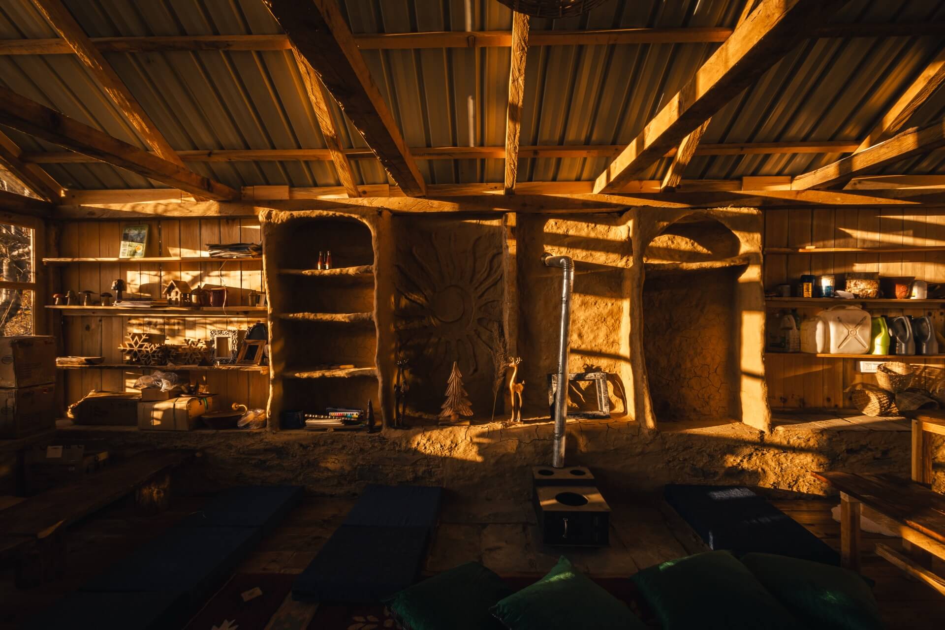 Mud-walled common space at Wild in golden-hour light, carved sun relief and wood stove