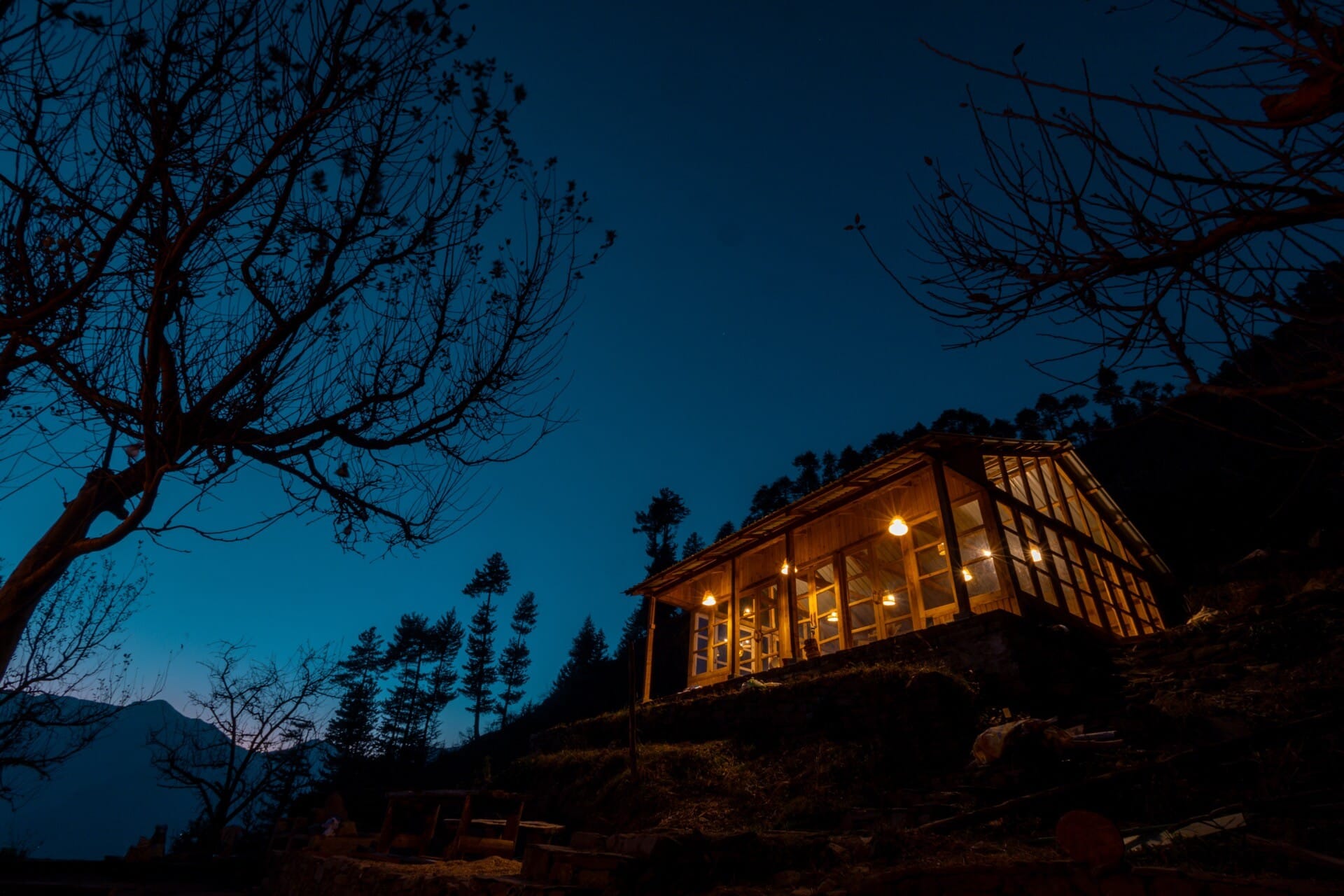 The cabin at Wild glowing warm against a deep-blue dusk sky — Jana, Himachal Pradesh