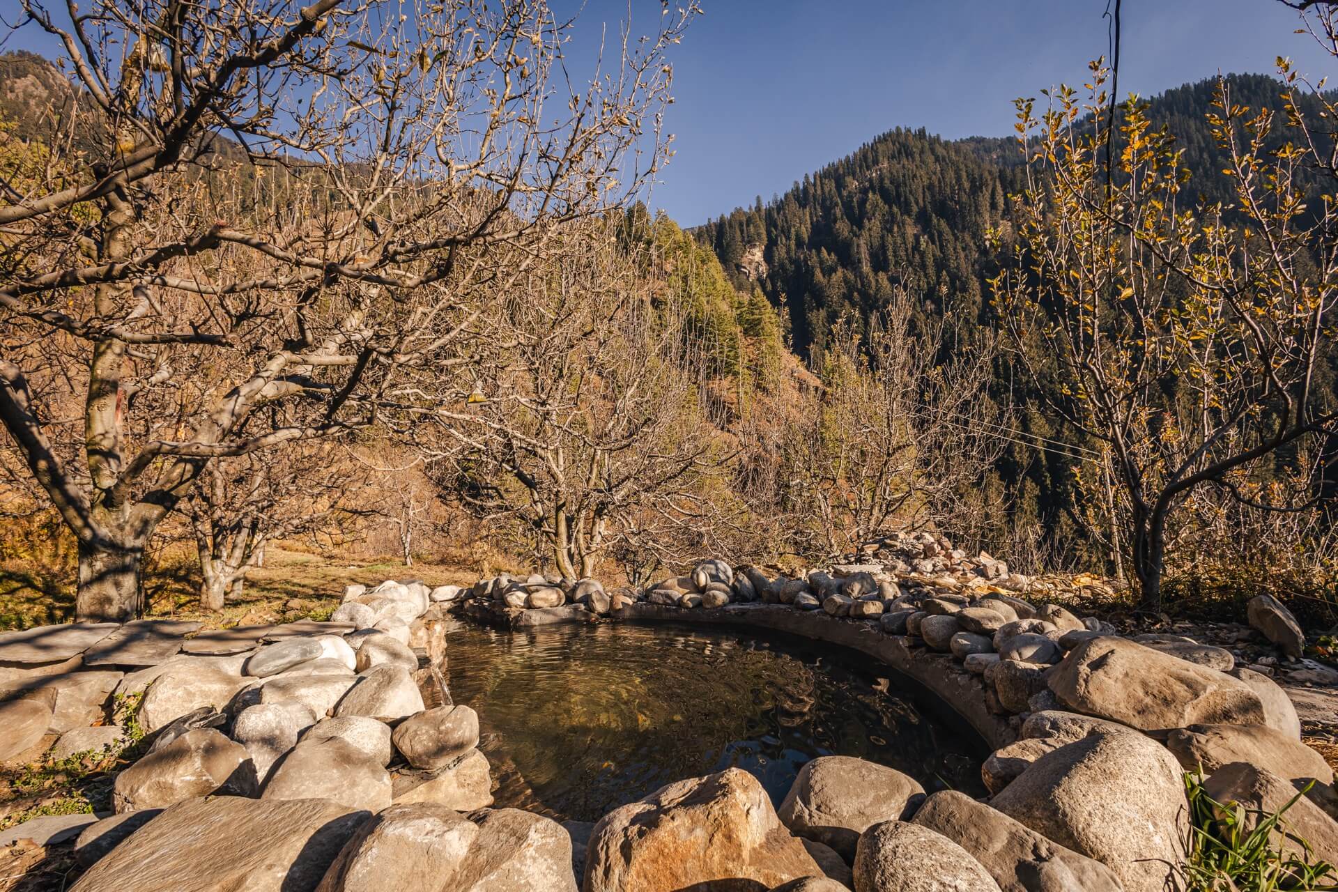 Snowmelt cold plunge ringed with stone at Wild, mountains behind