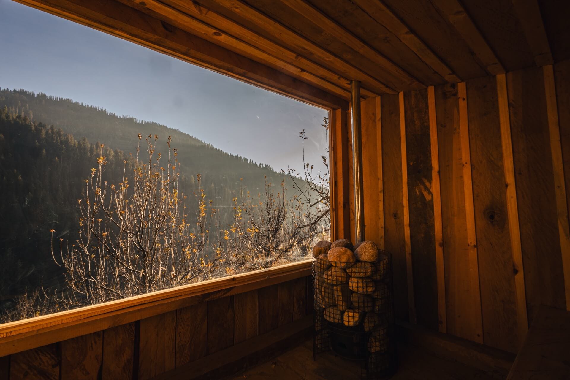 Sauna interior at Wild — heater and stones beside a wide mountain window